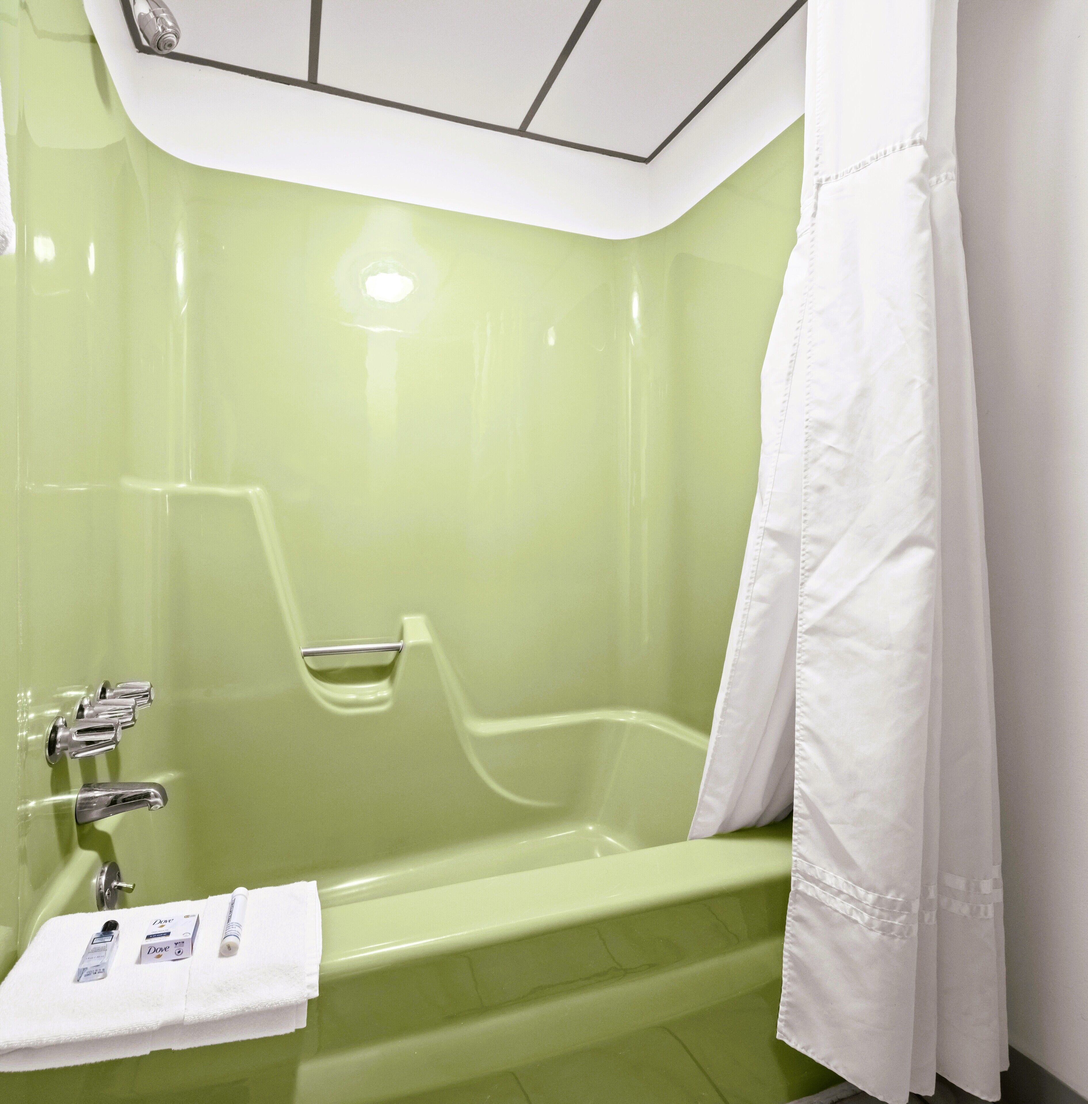 Un baño con una bañera verde, una cortina de ducha blanca y un perchero con artículos de aseo.