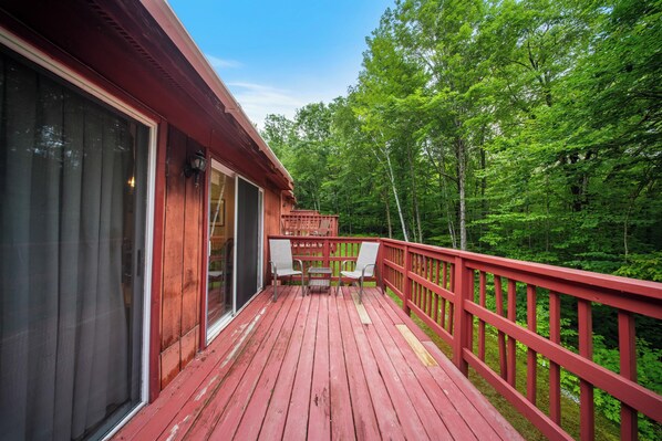 A wooden deck with red railings, two chairs, and a table.