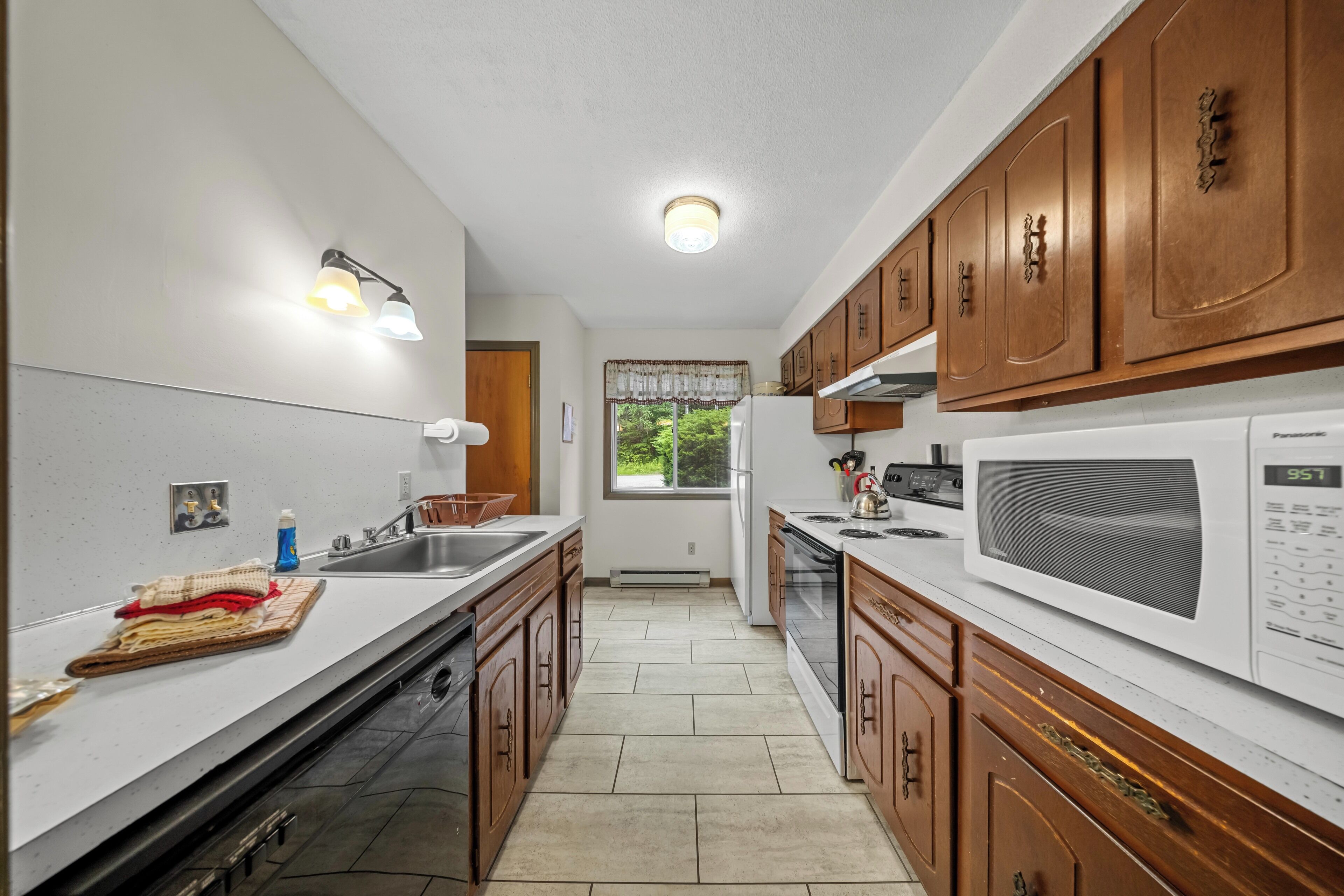 A kitchen with wooden cabinets, a white countertop, a sink, a stove, and a microwave.