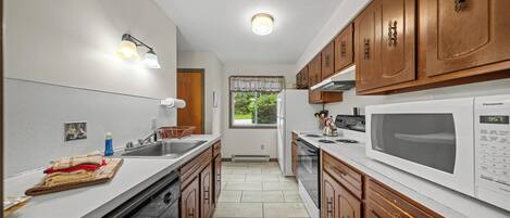 A kitchen with wooden cabinets, a white countertop, a sink, a stove, and a microwave.