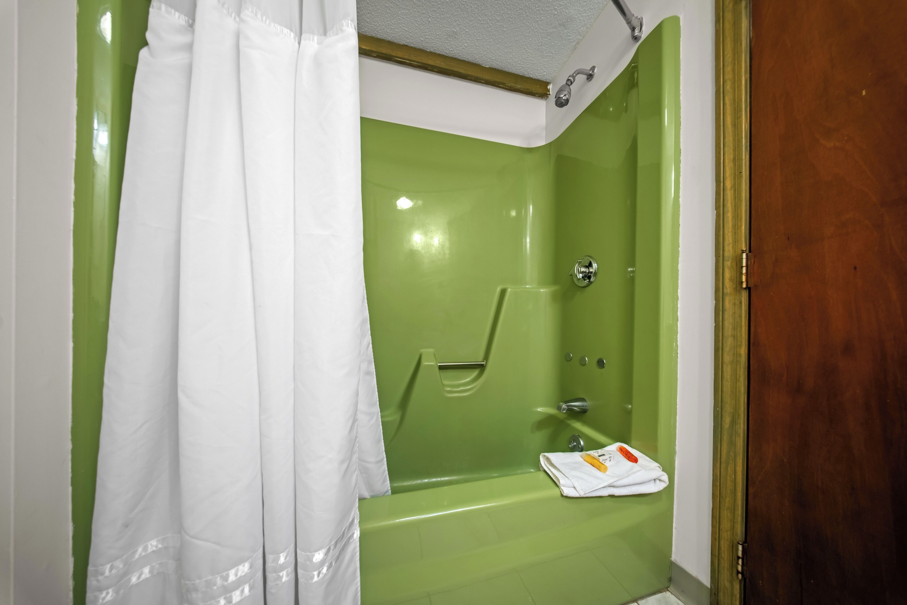 Um banheiro com uma banheira verde, um chuveiro com cortina branca e uma toalha no chão.