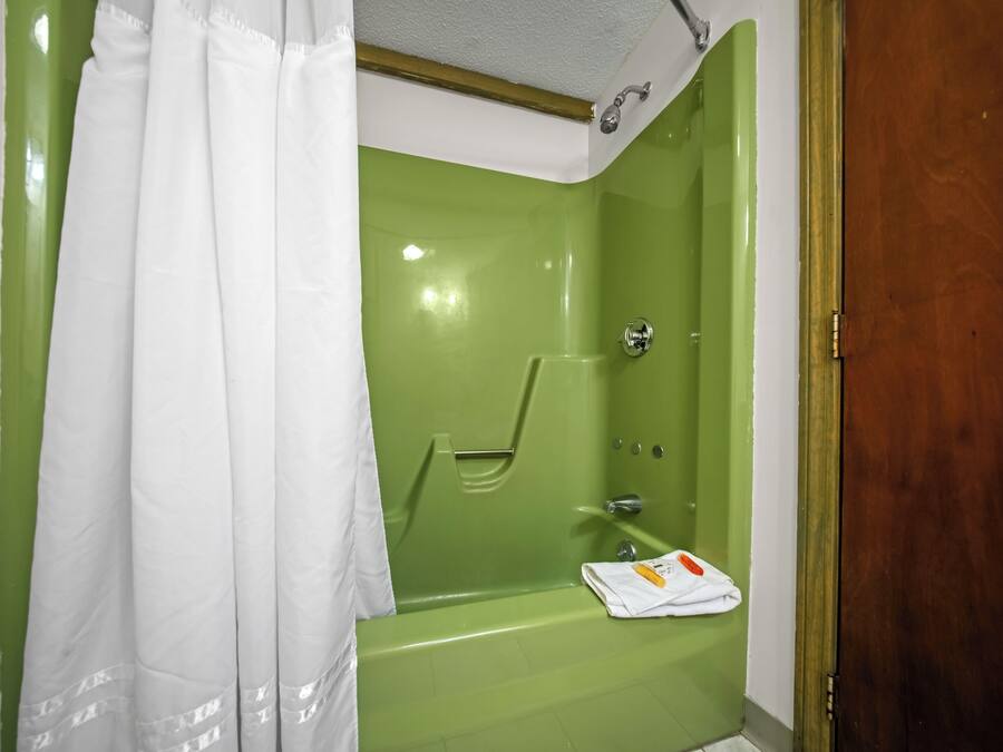 Um banheiro com uma banheira verde, um chuveiro com cortina branca e uma toalha no chão.