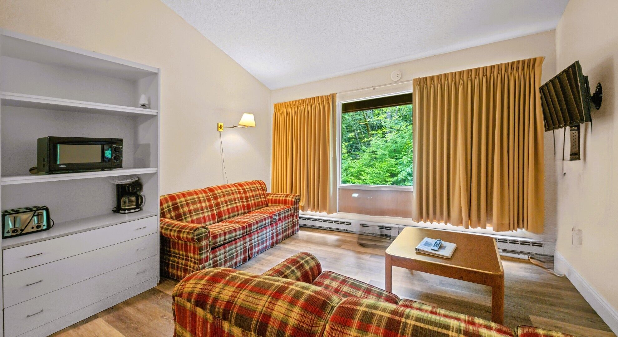 A compact living space with a sofa, a small table, a microwave, and a shelf with a coffee maker.
