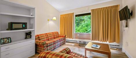 A compact living space with a sofa, a small table, a microwave, and a shelf with a coffee maker.