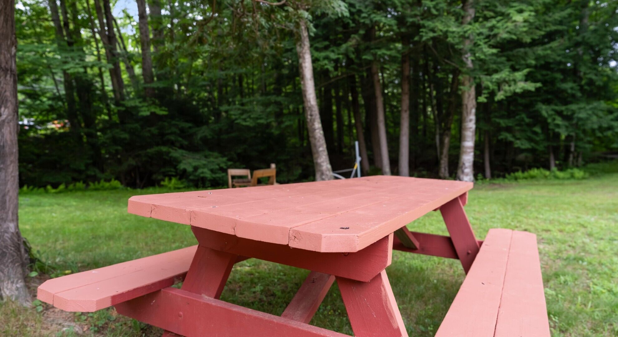 A red picnic table in a grassy area with trees in the background.