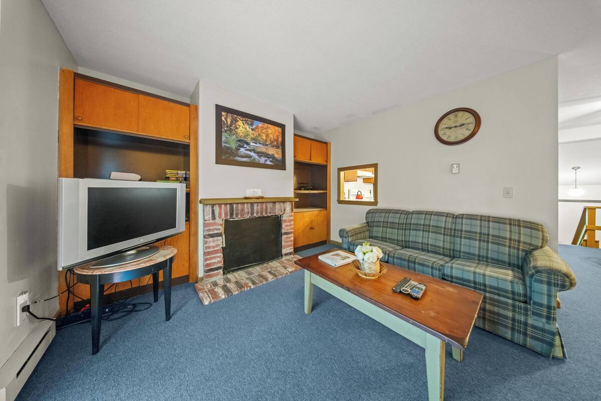 Uma sala de estar com televisão, lareira, sofá e um relógio na parede.