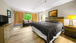 A modern bedroom with a large bed, a TV, a wooden dresser, and a view of greenery through the window. - Evergreen Valley Inn by Coolvacay (Stoneham)