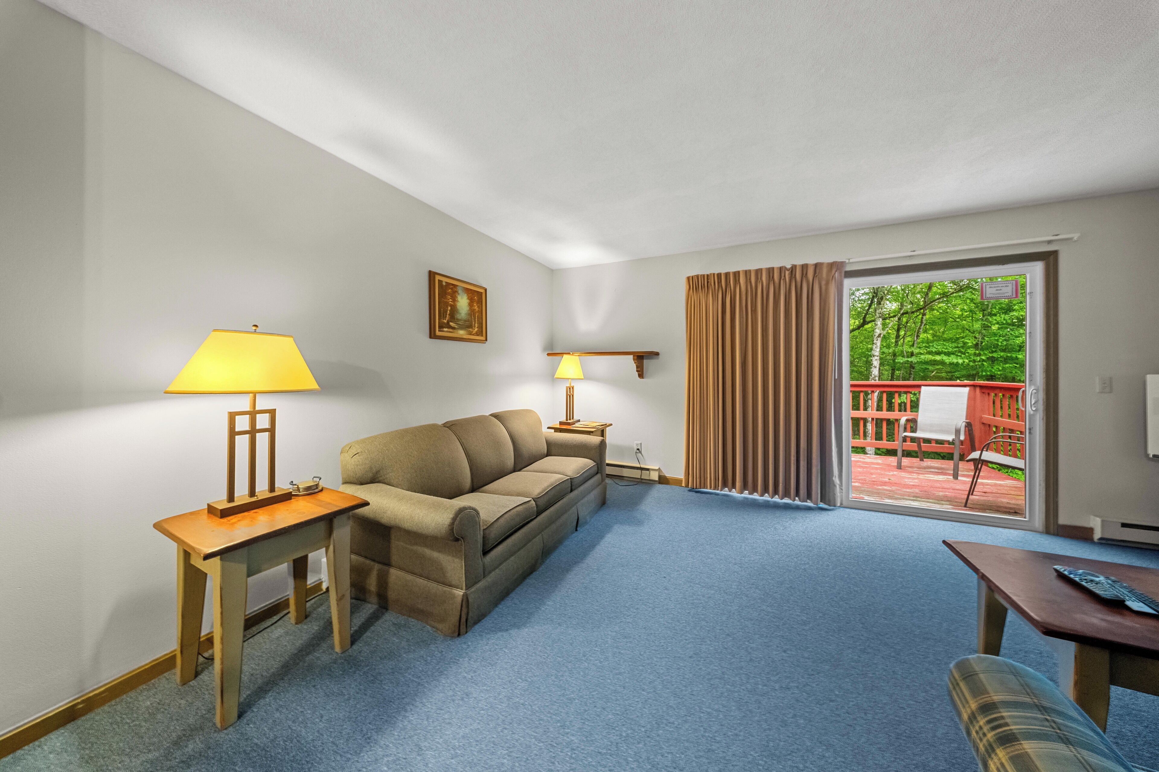 Una habitación con sofá, una mesita, una lámpara y vistas a un patio con mobiliario de exterior.