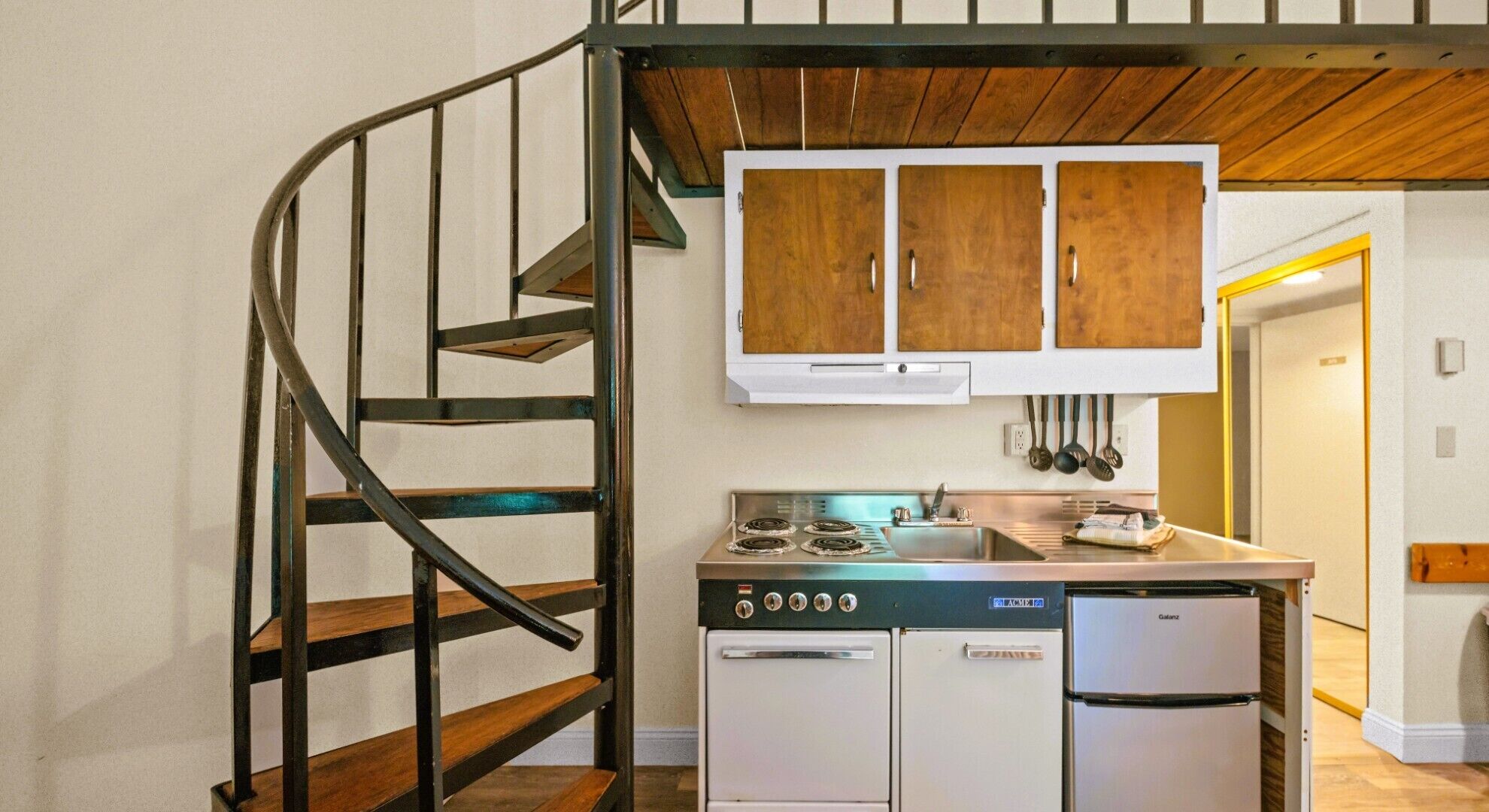 Eine Küche mit Herd, Backofen und Kühlschrank, einer Holztreppe und Schränken über der Arbeitsplatte.