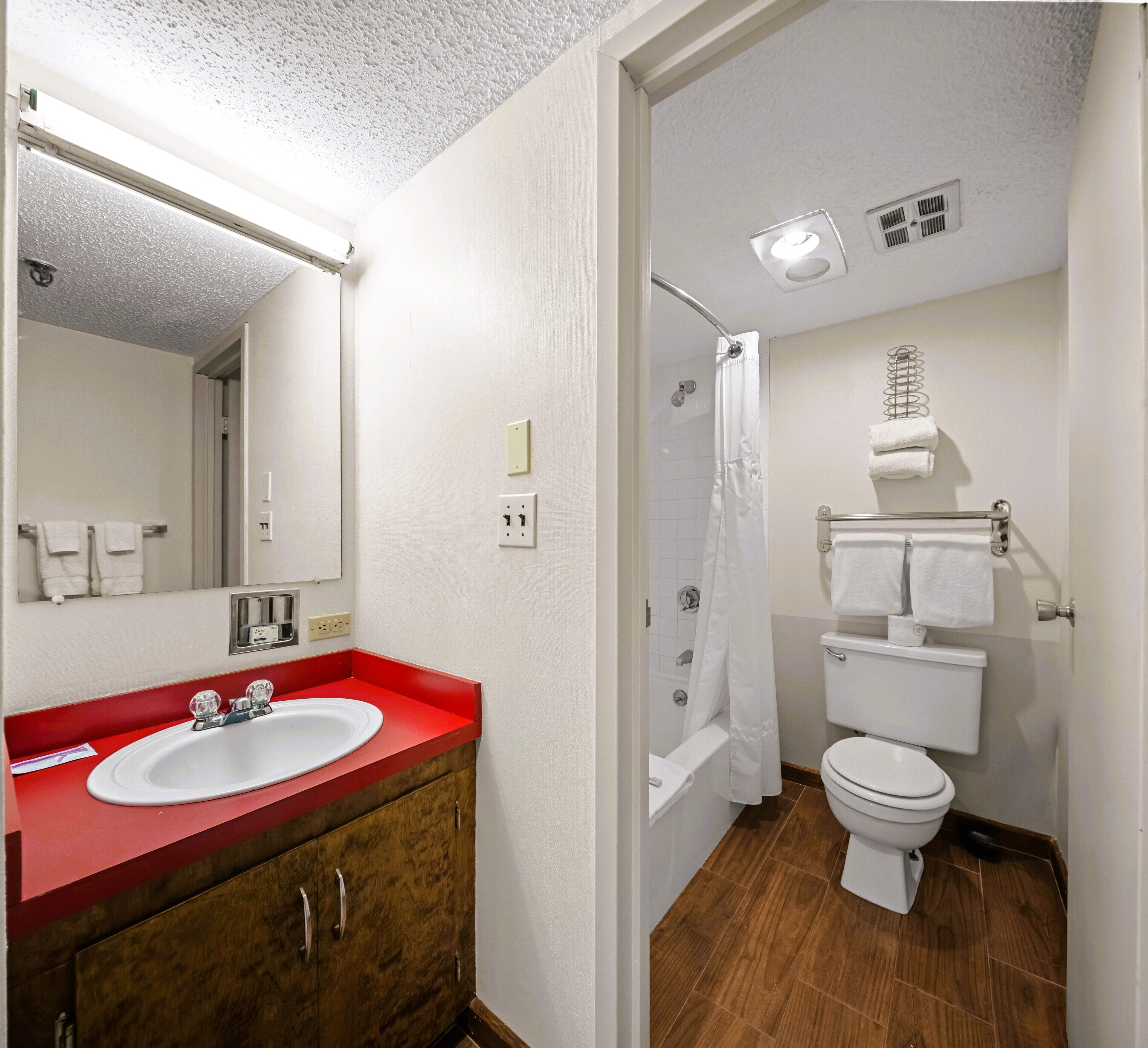 A bathroom with a red sink, white toilet, and shower curtain.