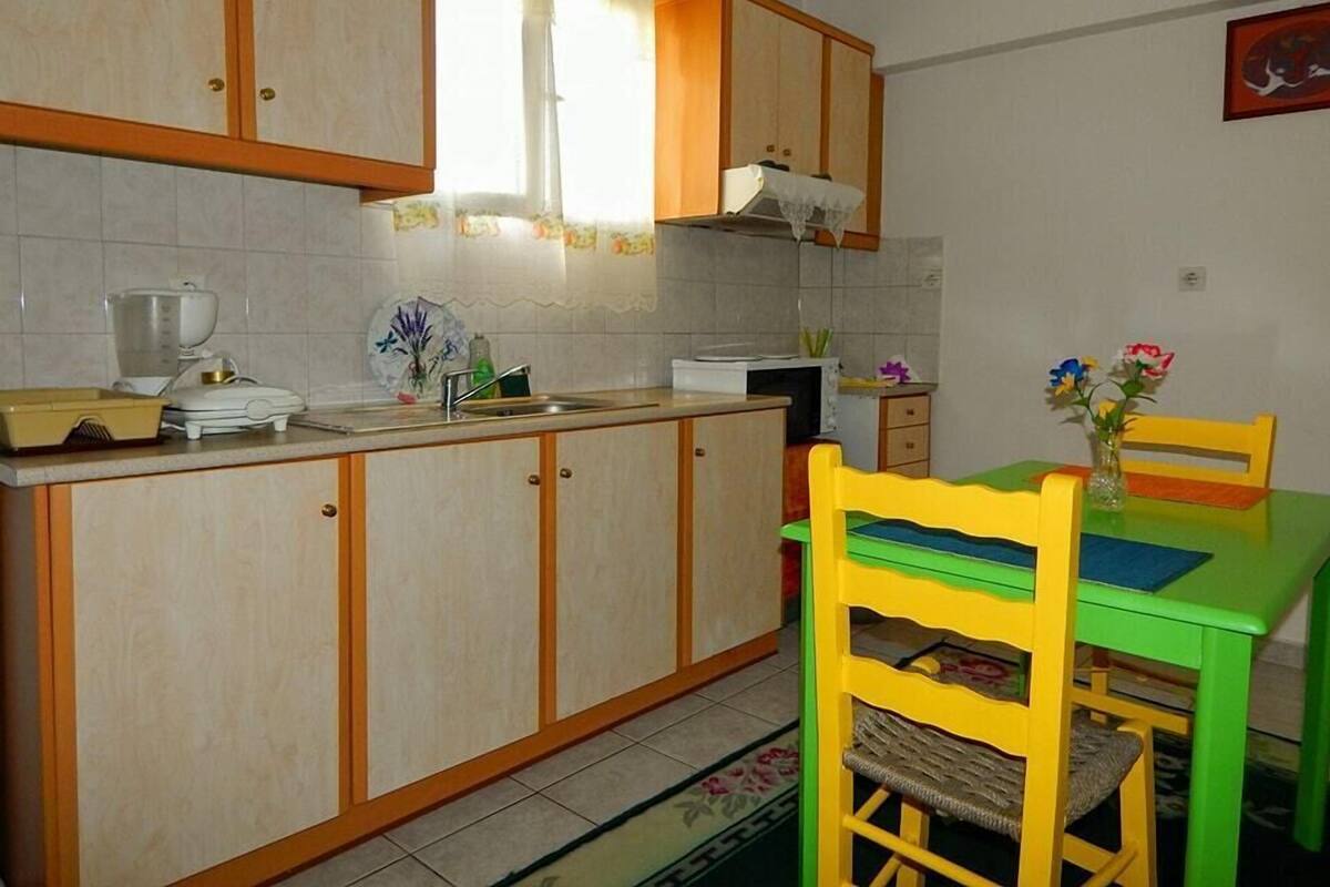 Una cuina petita amb armaris de fusta, un rentapeus i una taula de dinar amb caires.
