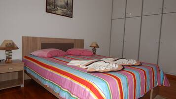 A bedroom with a wooden bed, striped bedding, two bedside lamps, a painting on the wall, and a wardrobe.