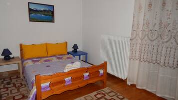 Un dormitorio con una cama de madera, una mesita de noche con lámpara, un radiador y un tapete estampado.