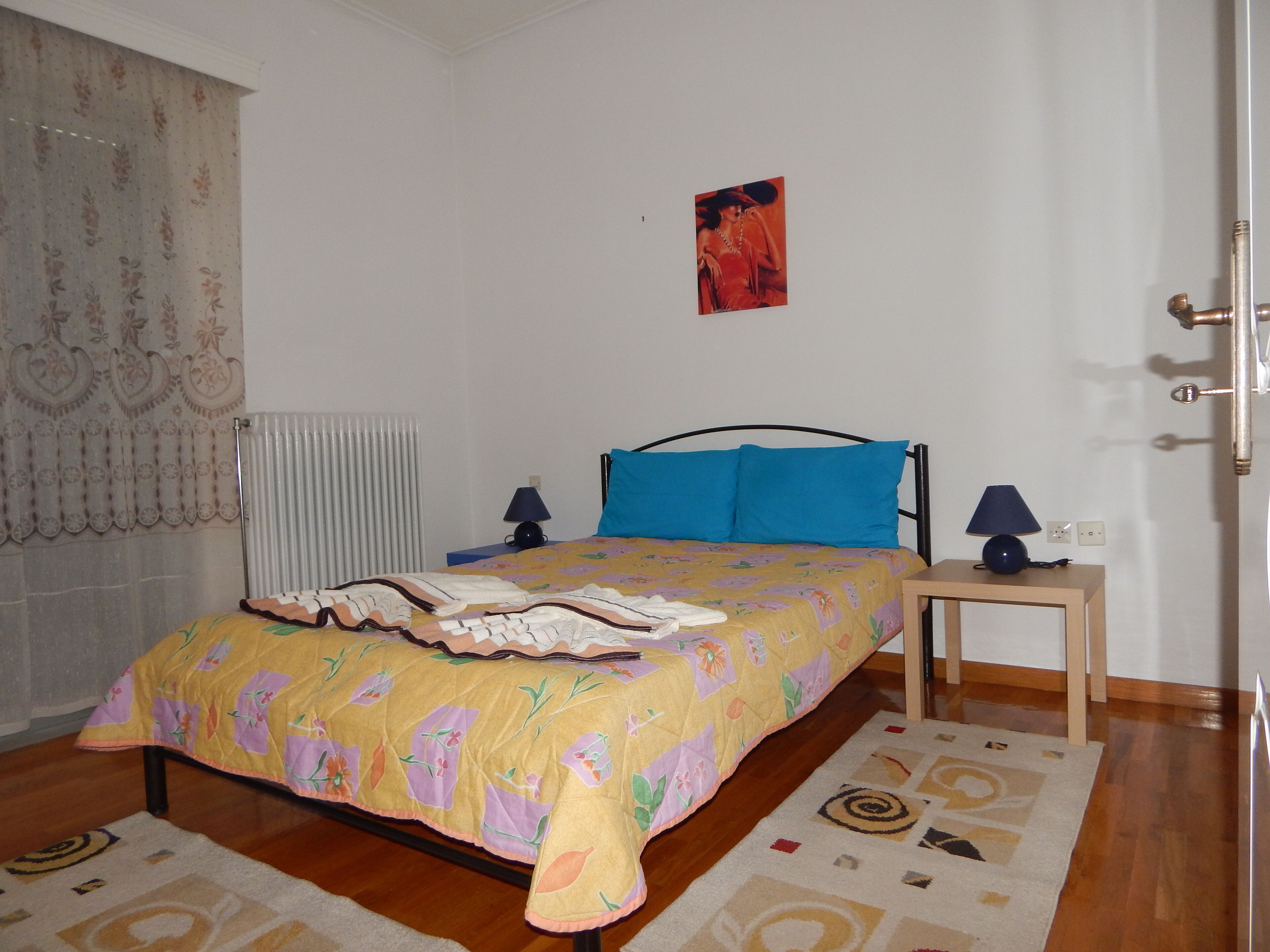 Un dormitorio con cama, mesita de noche, lámpara, radiador y puerta.