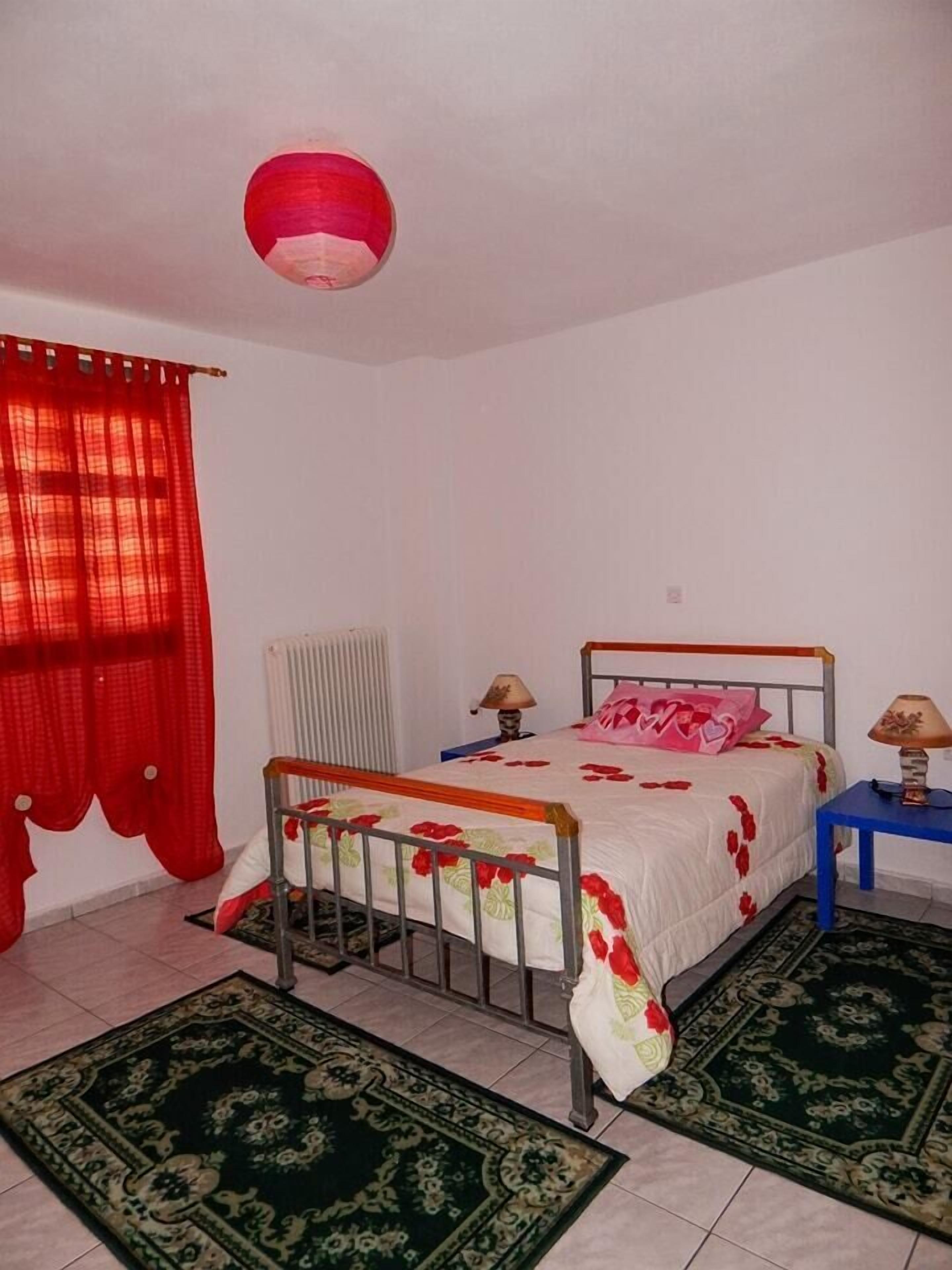 A bedroom with a bed, two bedside tables, a radiator, and a red curtain.