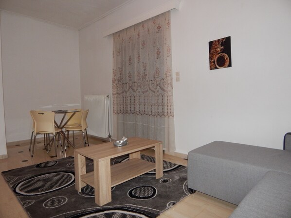 A small living room with a grey sofa, a wooden coffee table, and a dining table with chairs.