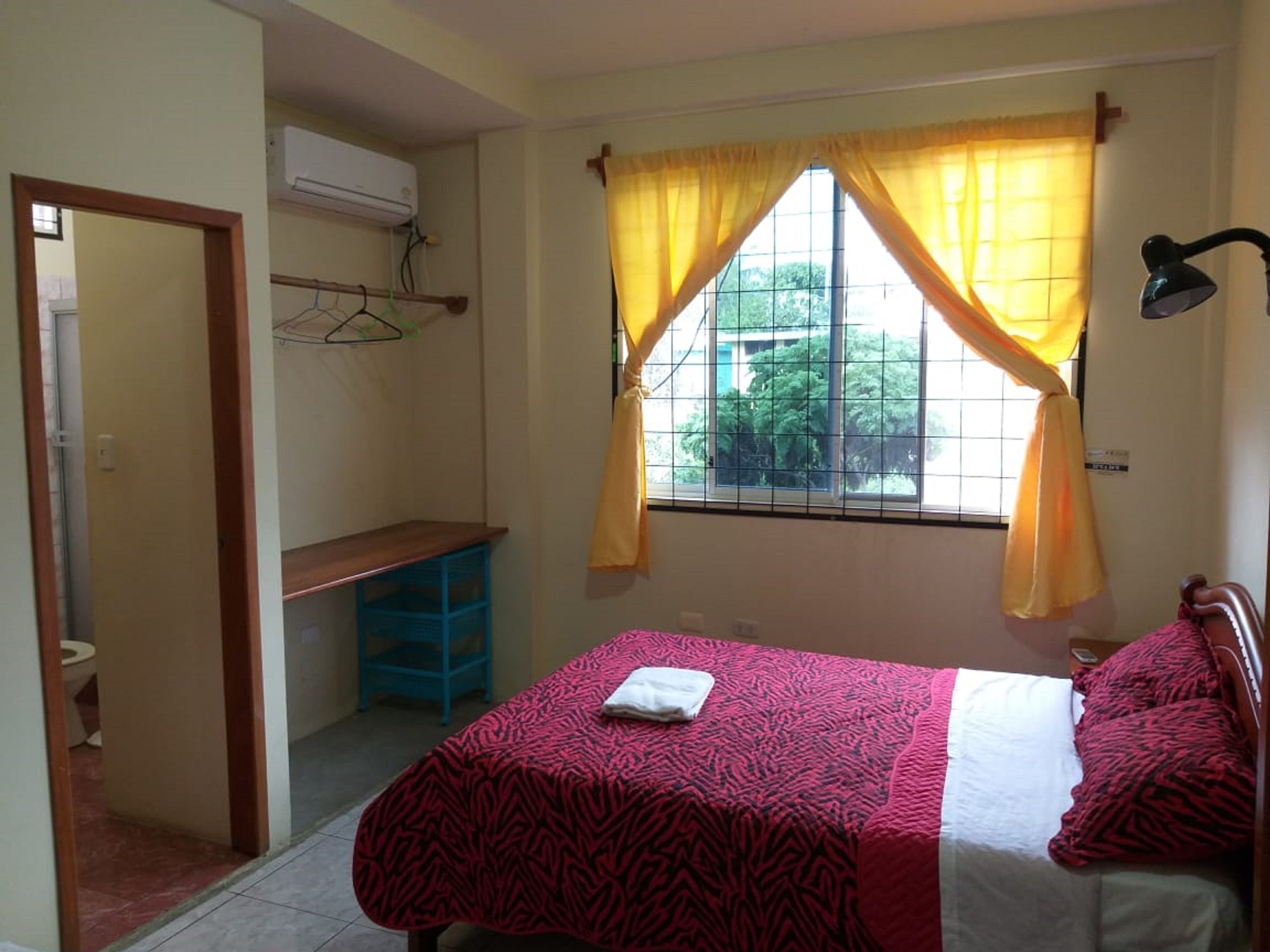 A bedroom with a bed, a desk, and a window with yellow curtains.
