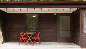 Eine Holzhütte mit einer kleinen Terrasse, einem Tisch und roten Stühlen.