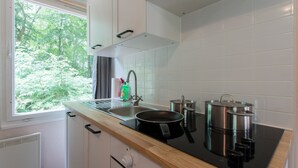 Eine moderne Küche mit einer schwarzen Induktionskochplatte, Edelstahlkochgeschirr, einer Spüle und einem Fenster mit Blick auf Grünflächen.