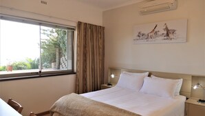 Ein Hotelzimmer mit Bett, Nachttischen, einem Schreibtisch und einem Fenster mit Vorhängen.