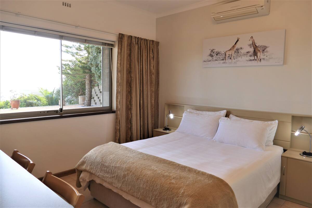 Una habitación de hotel con cama, mesitas de noche, un escritorio y una ventana con cortinas.