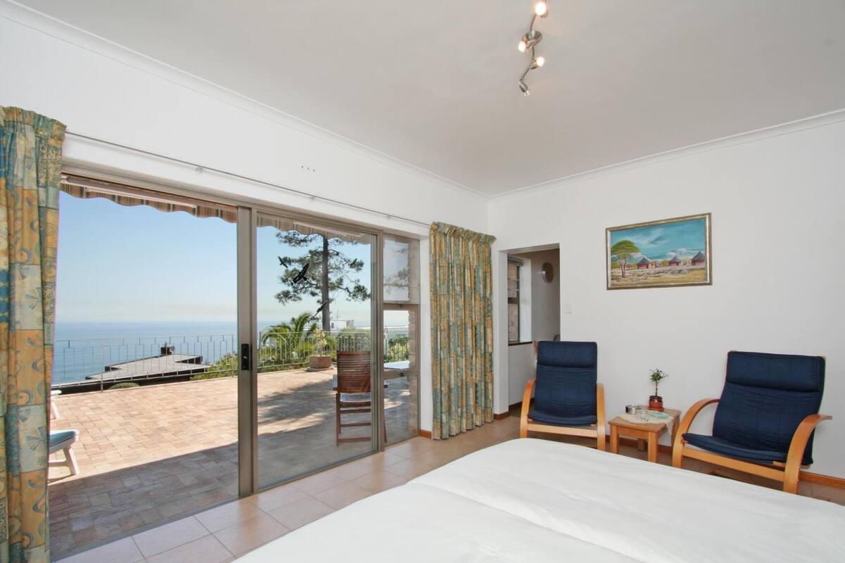 Habitación de hotel con cama, dos sillas, una mesita, un cuadro y vista al océano a través de una puerta corrediza.