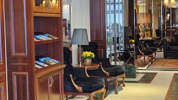 Een hal met een houten boekenkast, een zwarte beklede stoel, een lamp en een vaas met gele bloemen.