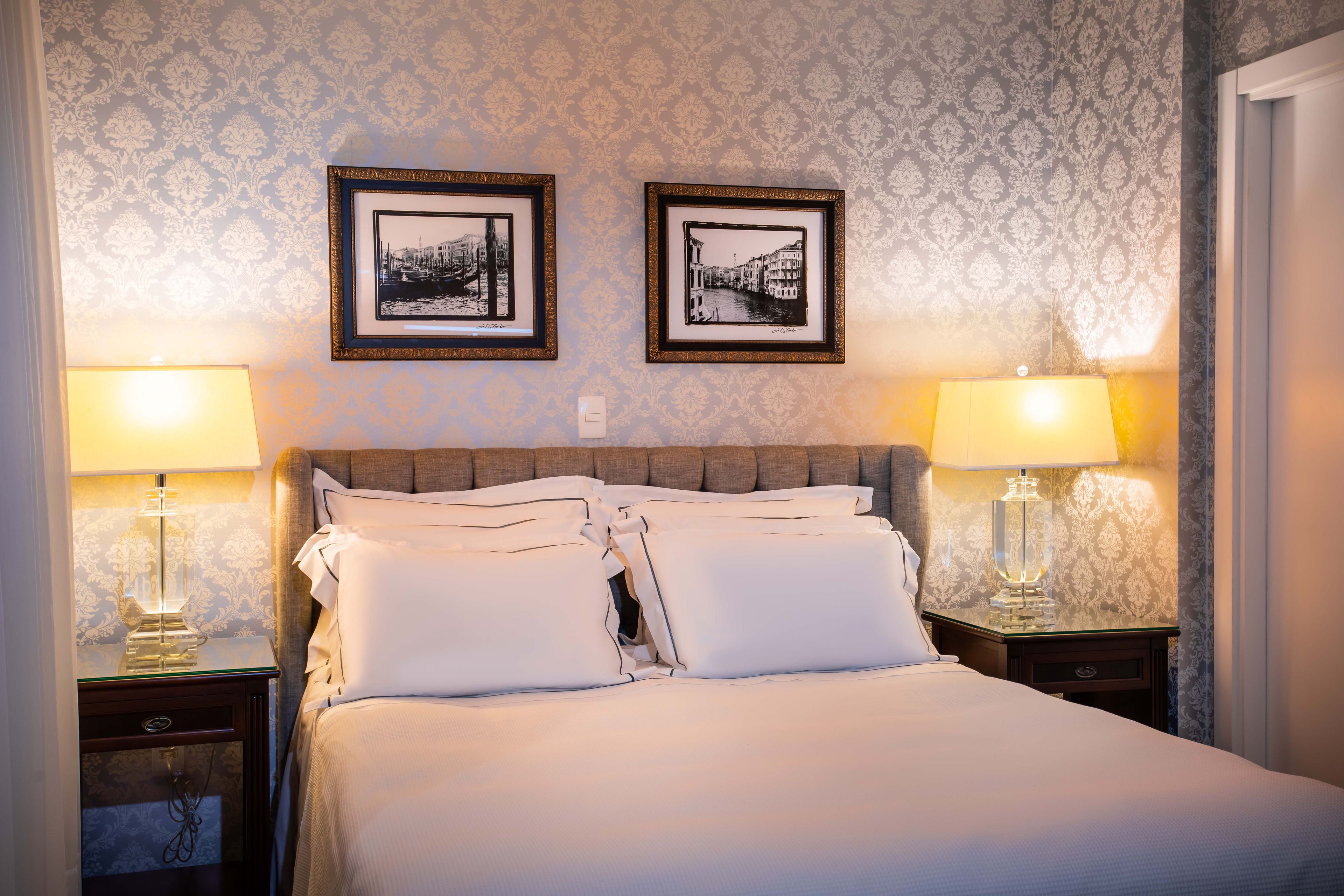 Habitación de hotel con una cama grande, dos lámparas de noche y dos cuadros en la pared.