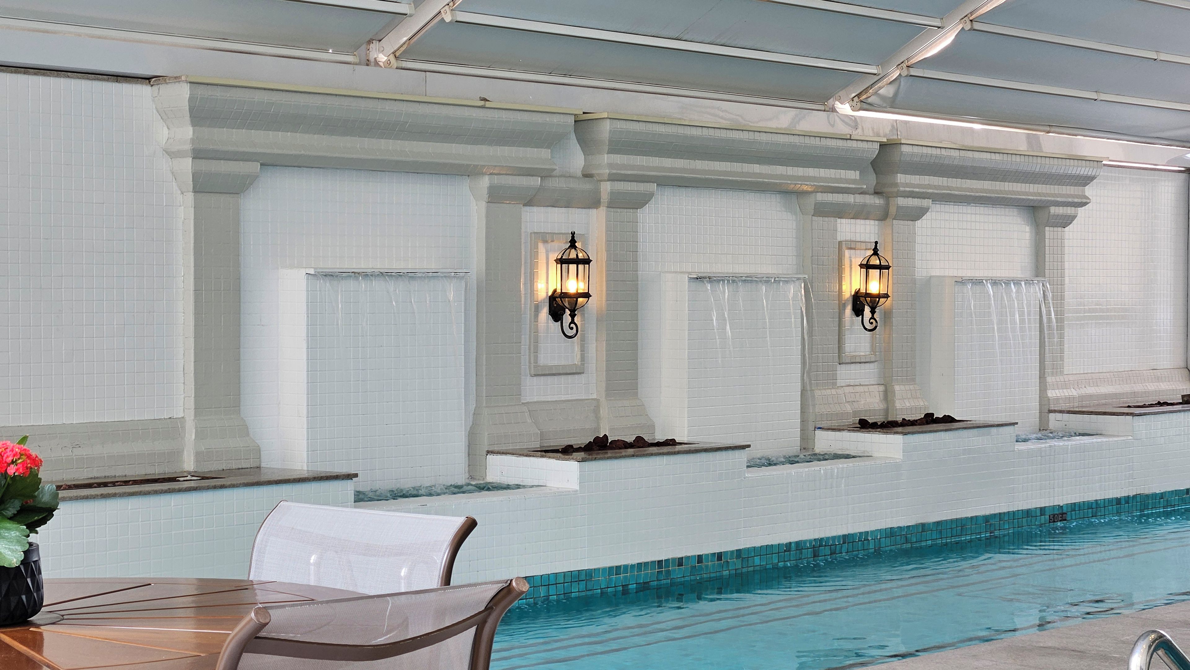A swimming pool with tiled walls and two wall-mounted light fixtures.