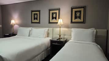 A hotel room with two beds, nightstands, lamps, and three framed awards on the wall.