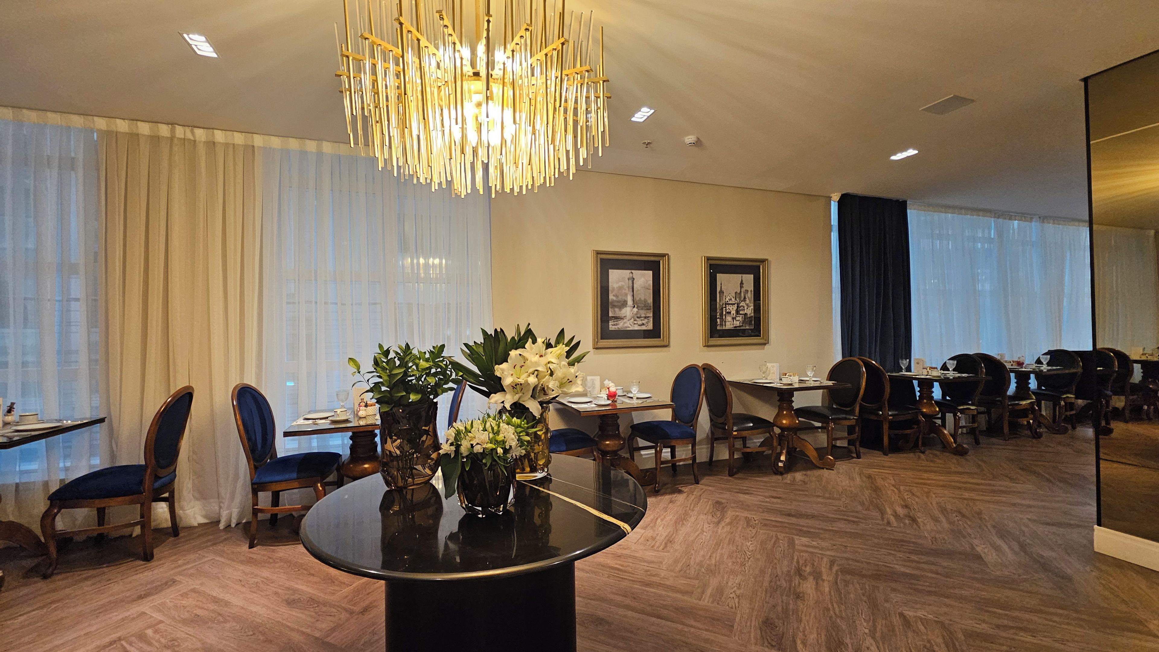 Un comedor de hotel con una lámpara de araña moderna, sillas de madera y una mesa redonda con un jarrón de flores.
