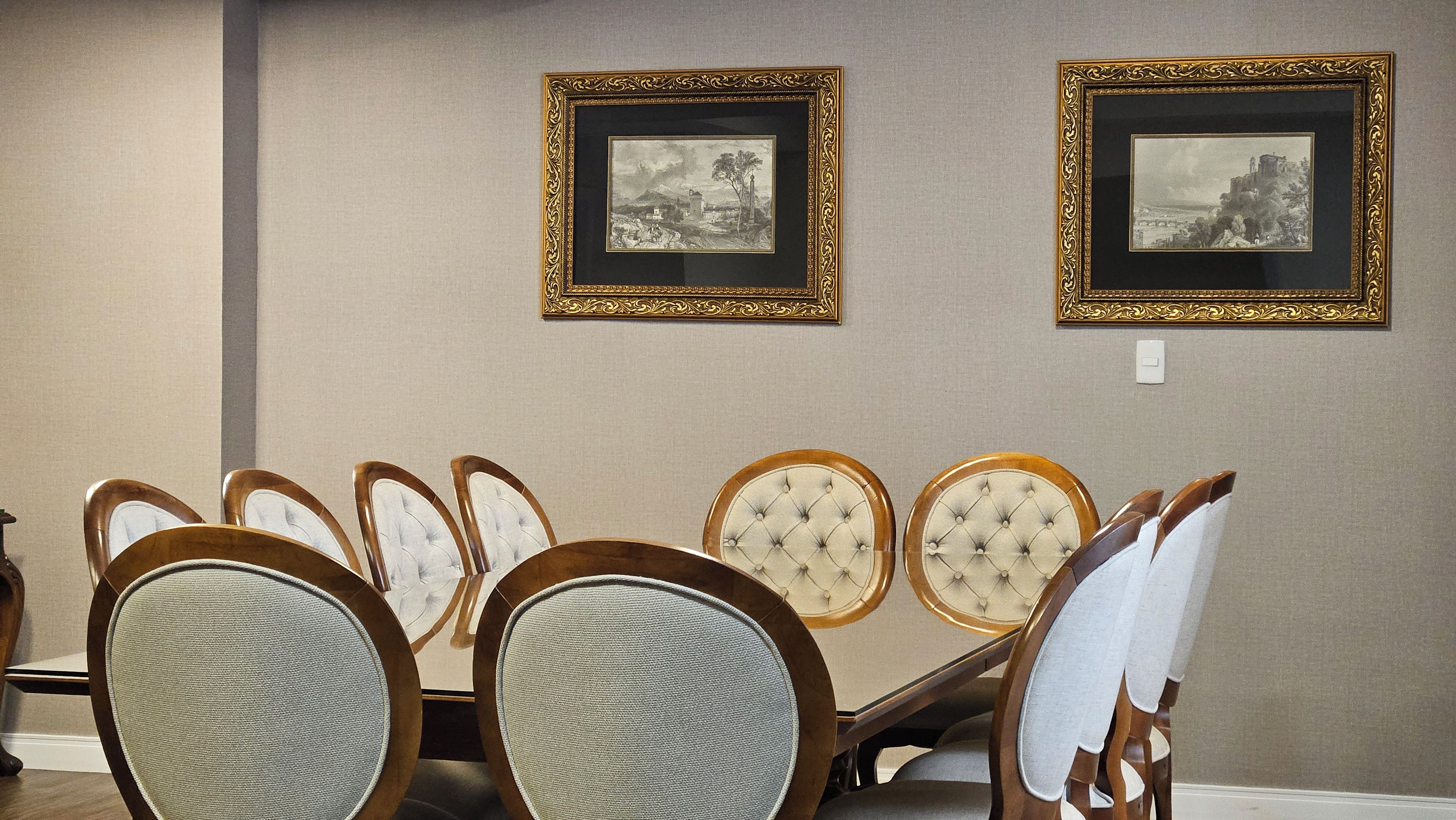 Un área de comedor con una mesa de madera y sillas tapizadas, dos fotografías en blanco y negro enmarcadas en la pared, y un interruptor de luz sobre la mesa.