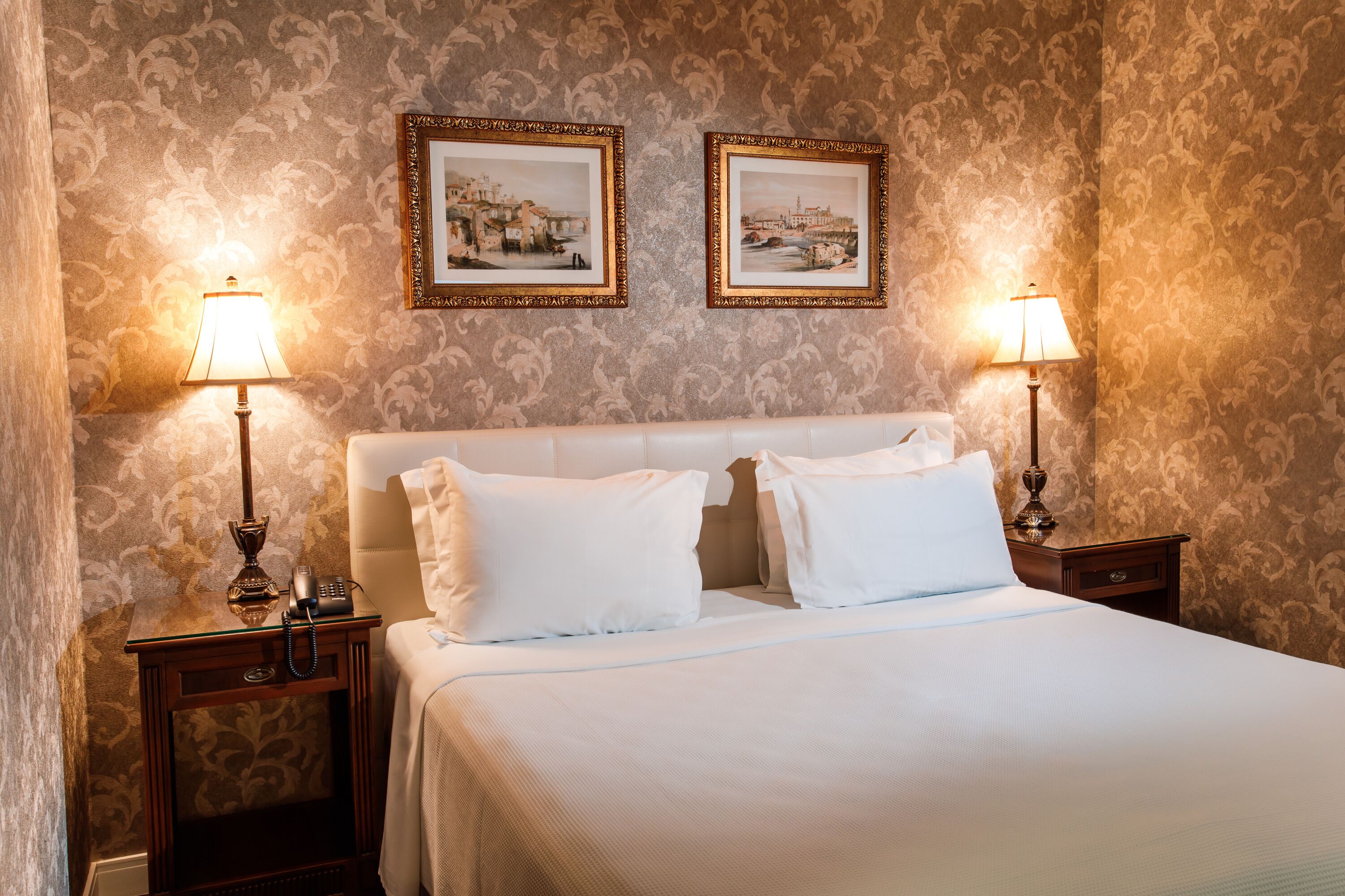 A hotel room with a large bed, two nightstands with lamps, and two framed pictures on the wall.