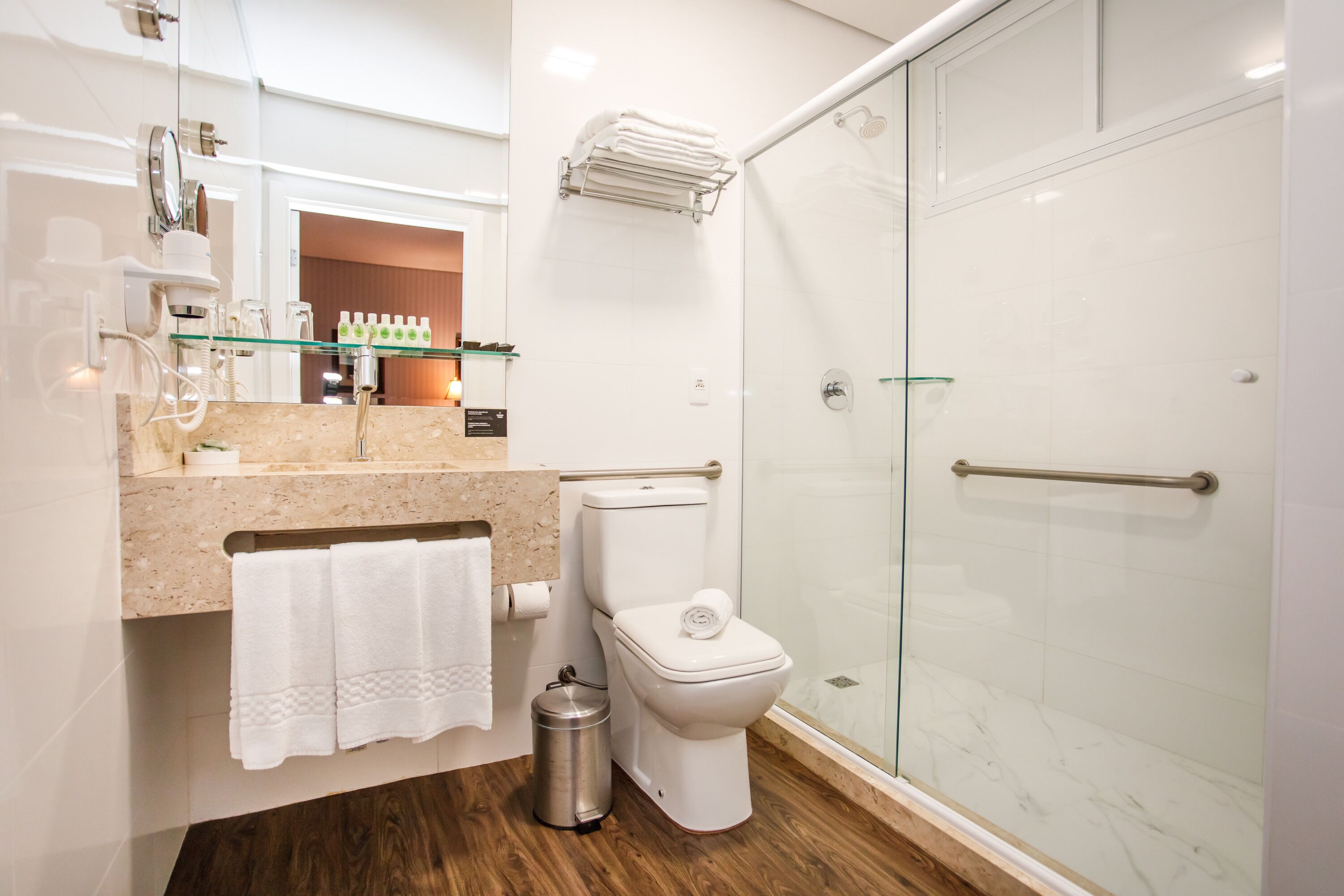 Ein modernes Badezimmer mit Duschkabine aus Glas, Toilette, Waschbecken mit Marmorplatte und Ablagefläche aus Glas darüber.