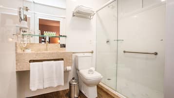 Ein modernes Badezimmer mit Duschkabine aus Glas, Toilette, Waschbecken mit Marmorplatte und Ablagefläche aus Glas darüber.