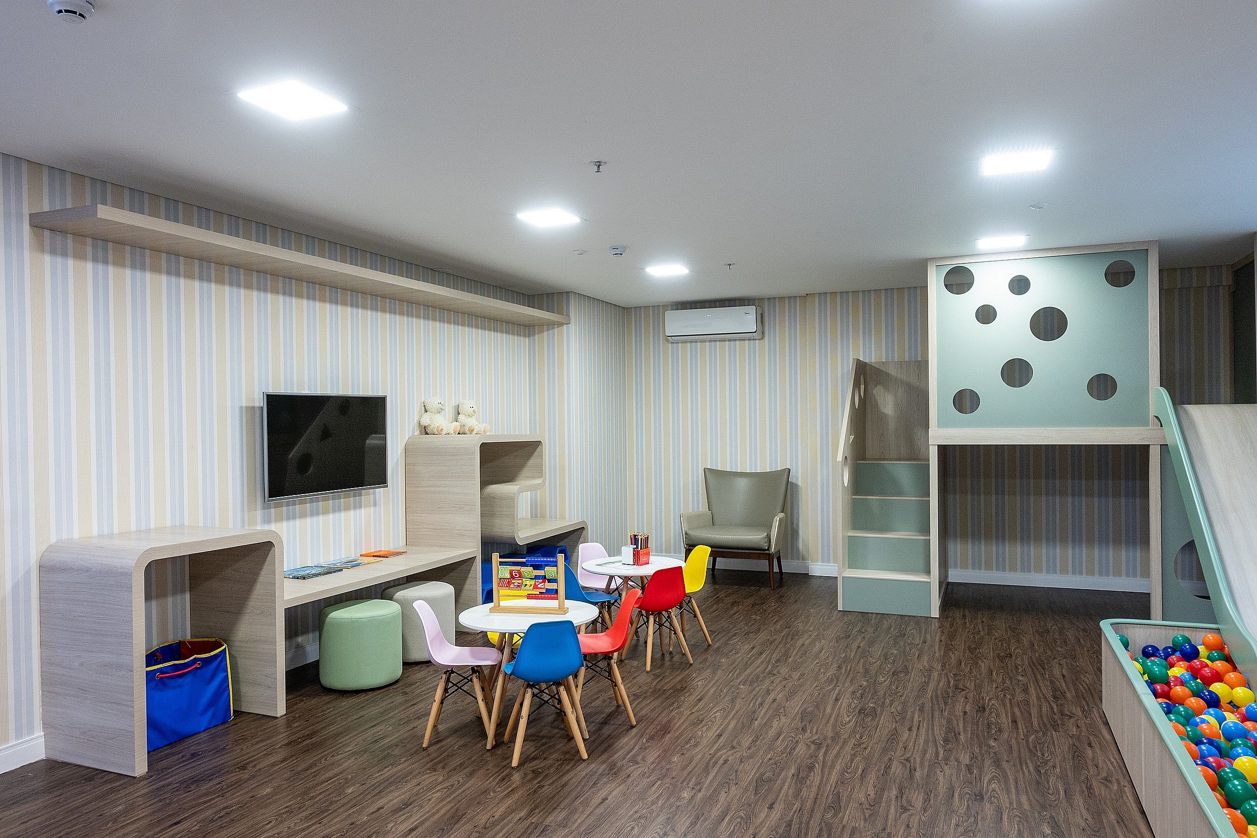 Una sala de juegos para niños con televisión, asientos, piscina de pelotas y un tobogán.