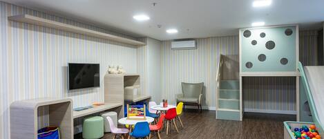 Una sala de juegos para niños con televisión, asientos, piscina de pelotas y un tobogán.