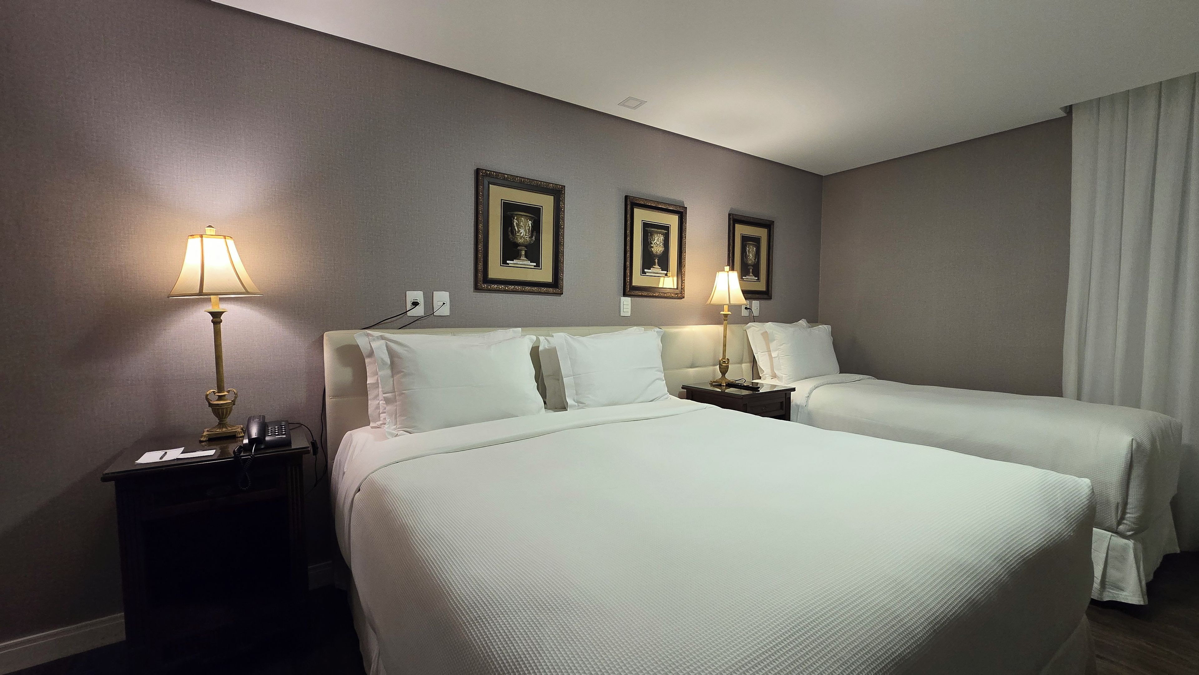 A hotel room with two beds, bedside lamps, a telephone, and framed pictures on the wall.
