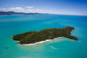 Vista aérea de una isla tropical con un mar turquesa cristalino, vegetación verde exuberante y una playa de arena.