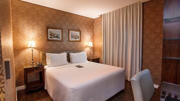 Una habitación de hotel con una cama grande, dos lámparas de noche, una mesita de noche, una silla y un armario de madera.