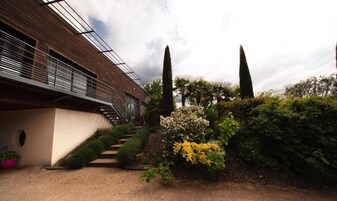 A modern building with a staircase leading to a covered area, surrounded by well-maintained greenery and tall trees.
