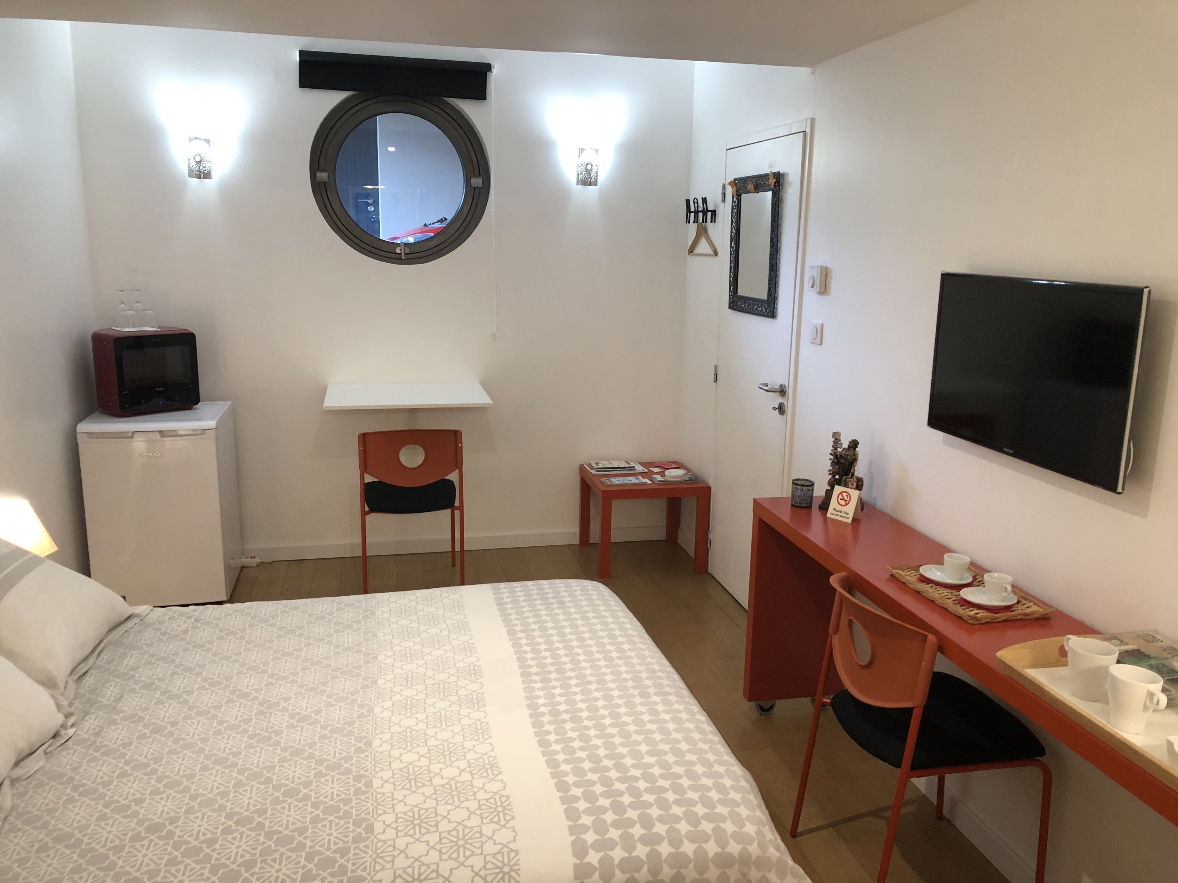 A hotel room with a bed, a desk, a chair, a television, a small refrigerator, a mirror, and a window.