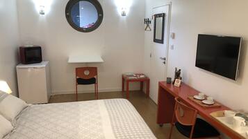 A hotel room with a bed, a desk, a chair, a television, a small refrigerator, a mirror, and a window.