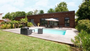Ein modernes Haus mit Swimmingpool, Sitzgelegenheiten im Freien und einer Holzterrasse.