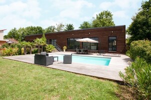 A modern house with a swimming pool, outdoor seating, and a wooden deck.