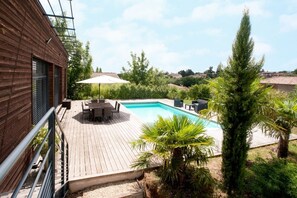 Una terraza de madera con piscina, mobiliario exterior y una palmera.