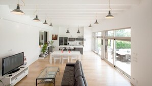 Ein modernes Wohnzimmer mit Sofa, Couchtisch und Fernseher, das in eine Küche und Essbereich mit großen Fenstern übergeht.
