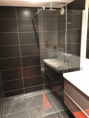 Un baño moderno con cabina de ducha de vidrio, un lavabo blanco y un espejo grande.