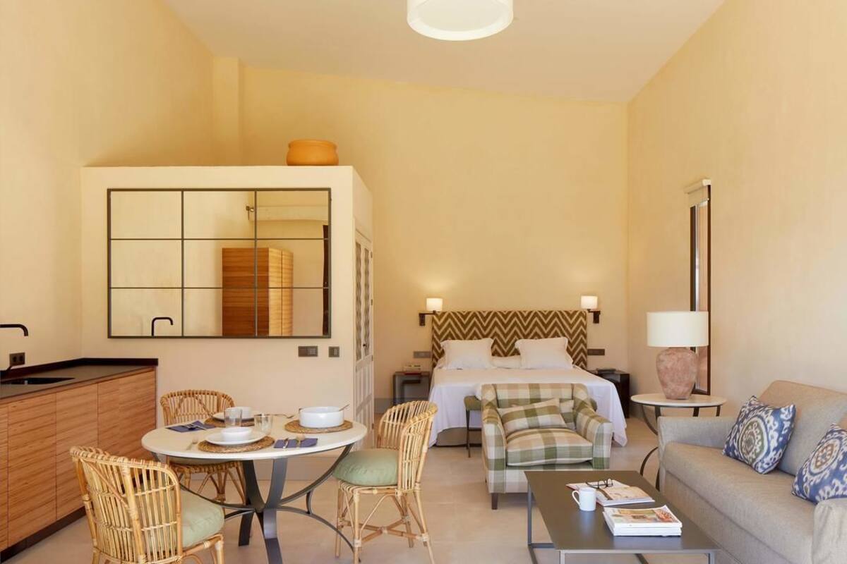 Habitación de hotel con cama, sofá, mesa de comedor con sillas, pequeña cocina y baño.