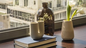 Une vue sur un paysage urbain avec un bâtiment historique perché sur une colline, une fenêtre avec un vase et un livre posés sur une table.